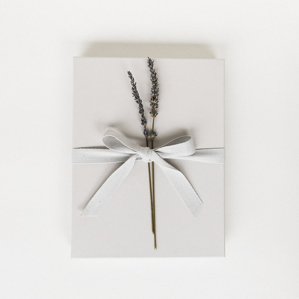 Dusty grey gift box with a ribbon and lavender flowers.