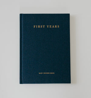 Deep navy linen minimal baby record journal. The cover says "First Years, Baby Record Book" in gold foil stamping.